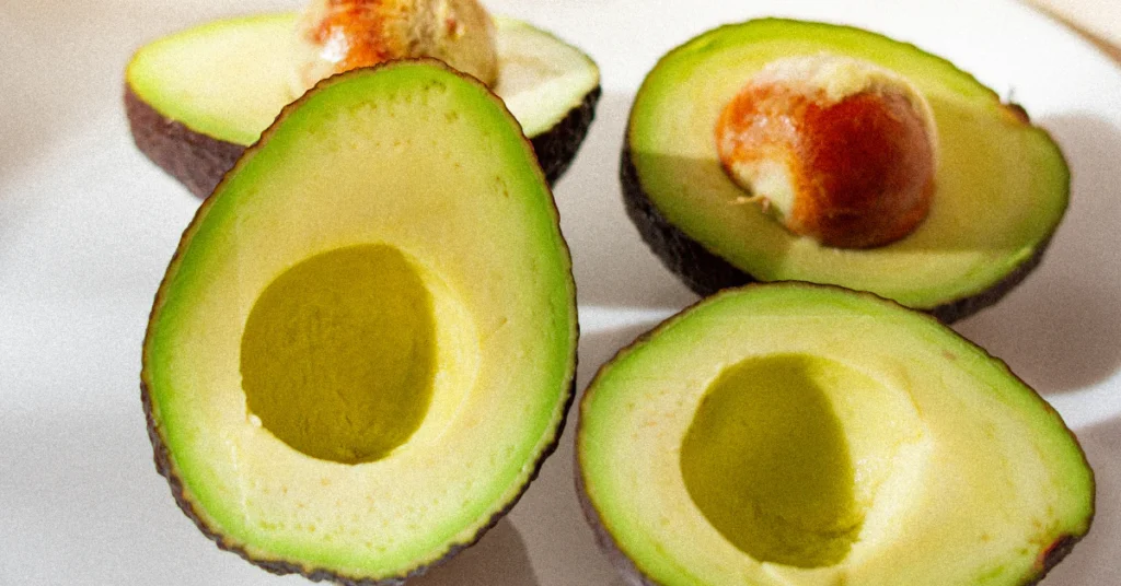 Avocado pit, skin, and sliced flesh laid out separately on a cutting board
