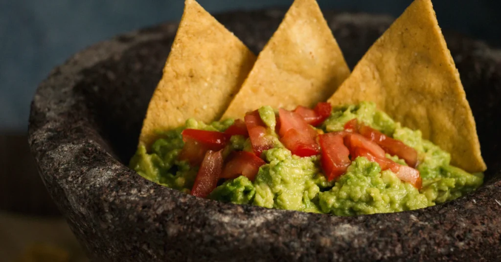 Bowl of guacamole with tortilla chips on a table just out of reach of a dog