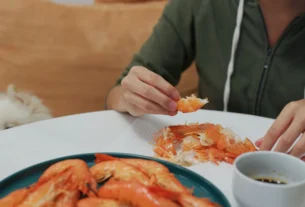 Person eating a plate of cooked shrimp at the table, showing whether dogs can have shrimp