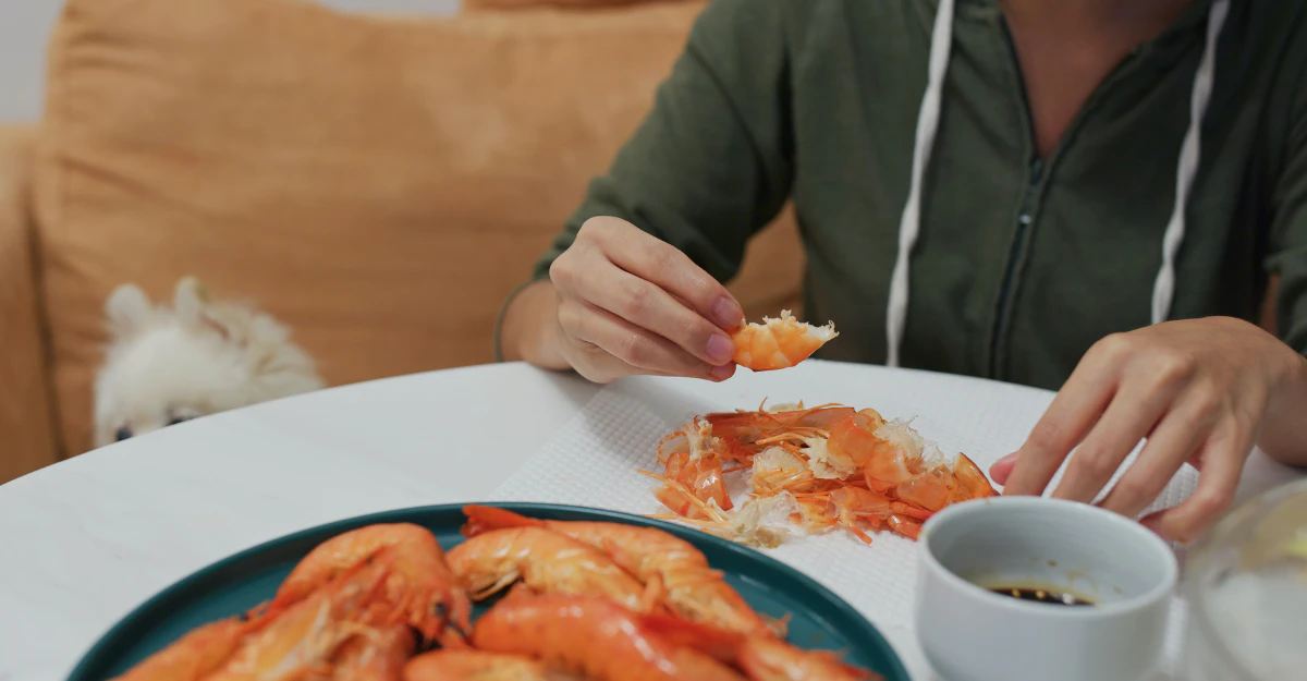 Person eating a plate of cooked shrimp at the table, showing whether dogs can have shrimp