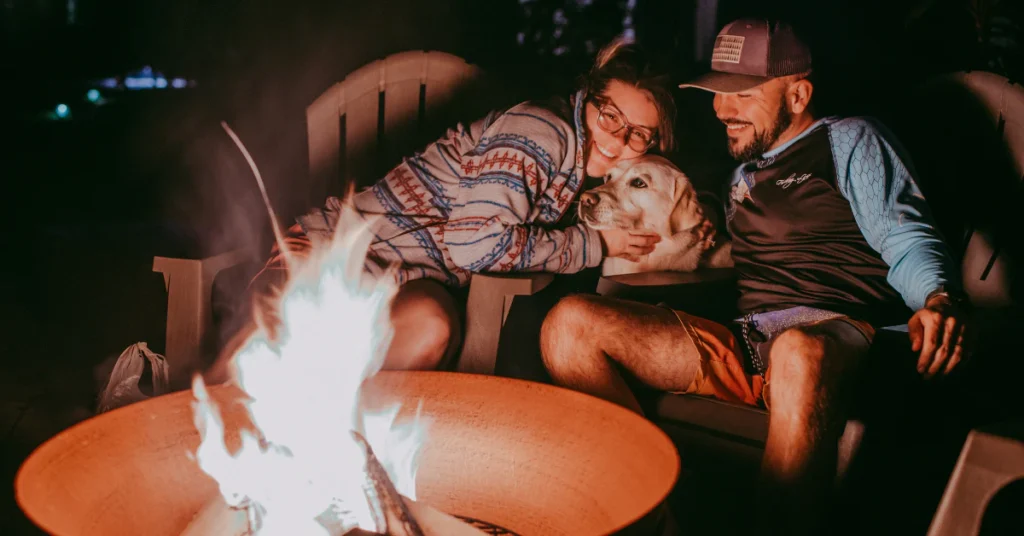 Family and pet sitting together by a glowing campfire in the evening
