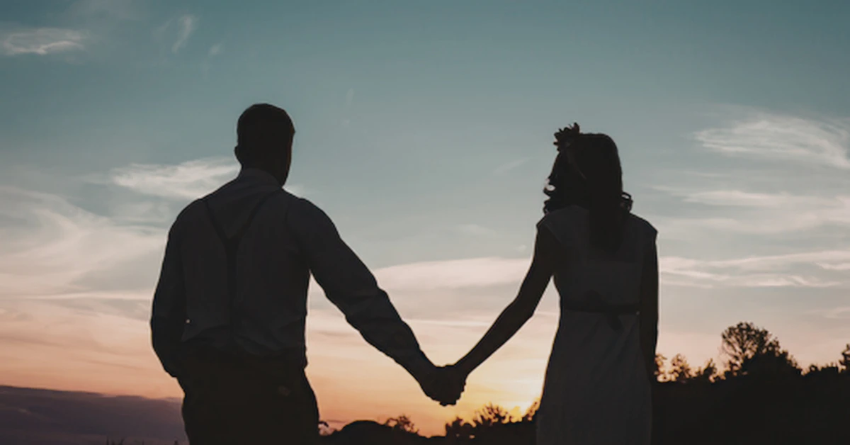 Silhouette of a couple holding hands while standing together at sunset